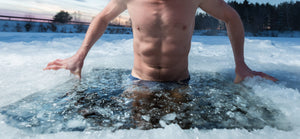 Man lowering his body into icy water in a outdoor ice hole in winter